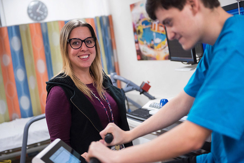 a patient in the cardiac fitness program rides a bike as a clinician looks on