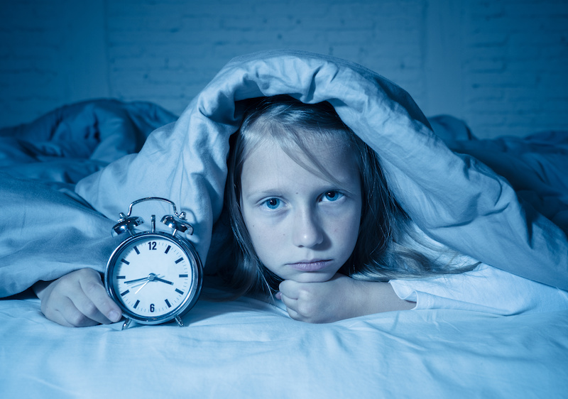 Girl awake in bed with alarm clock