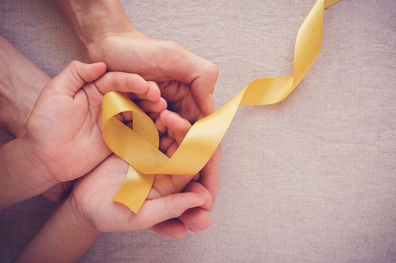 Adult and child hands holding yellow gold ribbon