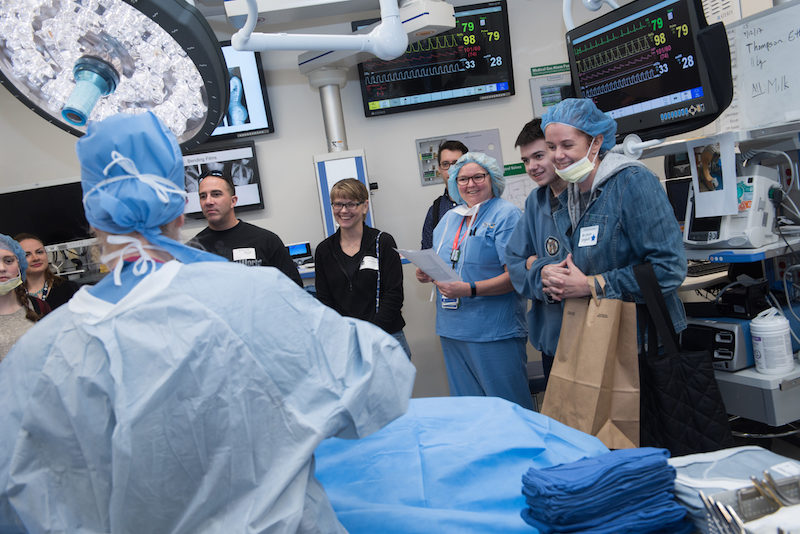 A clinician in a simulated operating room describes spinal fusion surgery for a group of patients and their families.