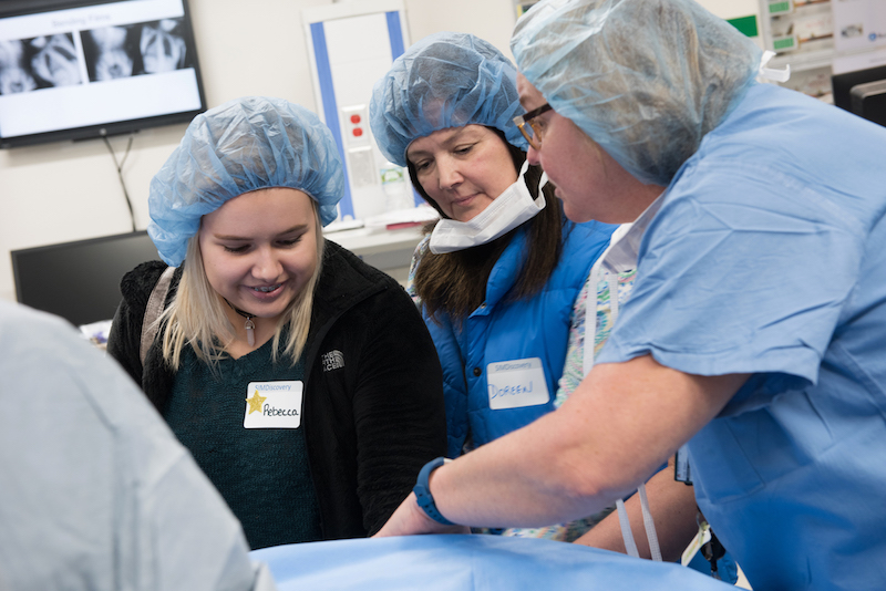 A nurse in the simulation lab shows a patient scheduled for spinal fusion surgery and her mother the surgical table. 