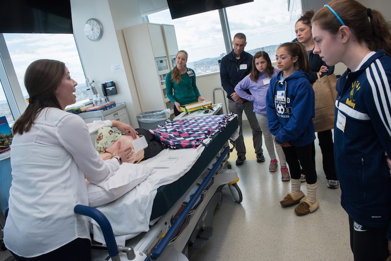 A nurse uses a mannequin in the simulation lab to show a group of patients what the bandages on their backs will look like after spinal fusion surgery.