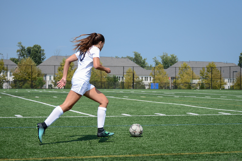 Female soccer player sprinting with the ball toward goal