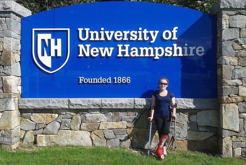 Lauren smiles in front of a large University of New Hampshire sign.