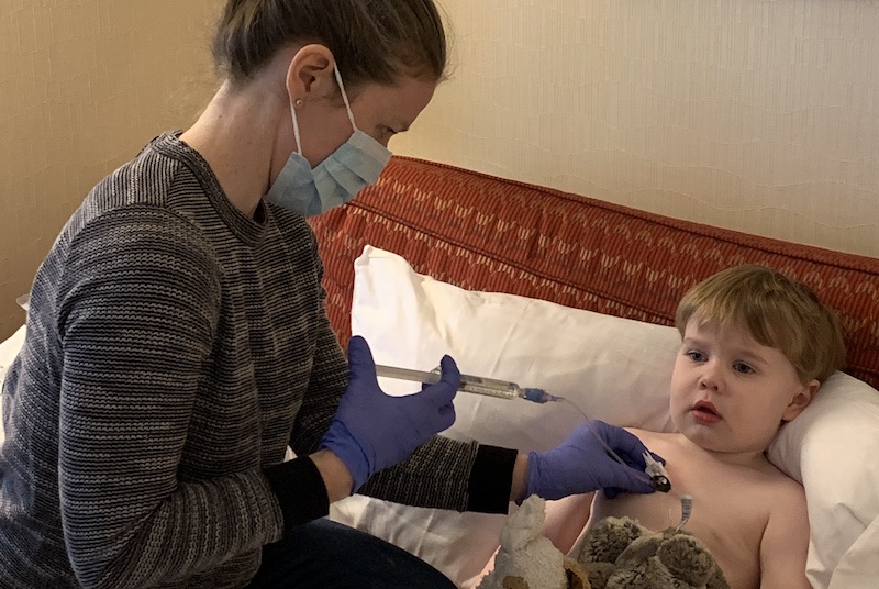 Colin, who has hemophilia, watches TV while his mother gives him an infusion.