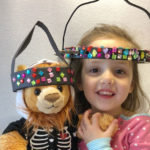 Gracie poses with a stuffed bear, both wearing surgical halos used during traction to repair severe spinal deformities.