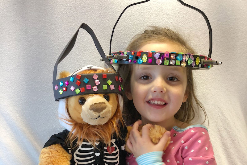 Gracie poses with a stuffed bear, both wearing surgical halos used during traction to repair severe spinal deformities.
