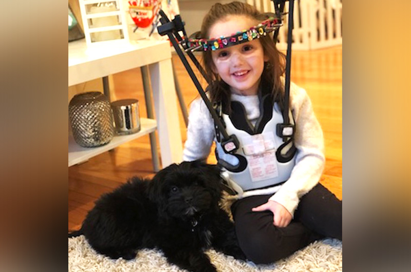 Gracie, wearing a halo vest after spinal fusion surgery, relaxes at home with her new puppy. 