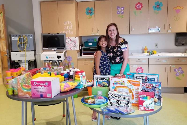 Liyana, who has epilepsy, poses with her child life specialist in front of donations she has collected for other children.
