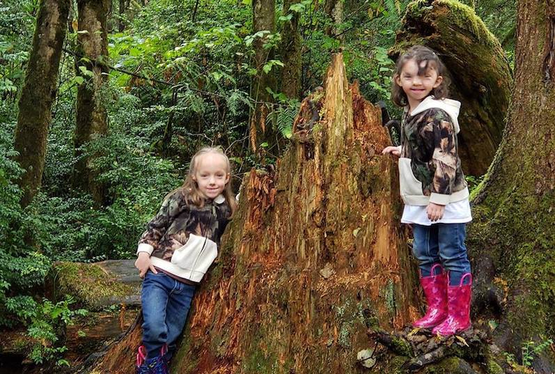 Violet, who had surgery for a craniofacial anomaly, poses in the woods with her twin sister