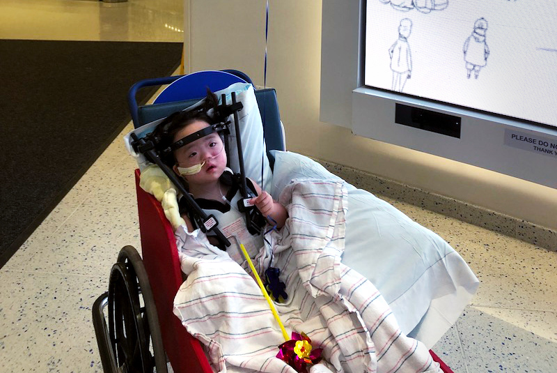 Everli, who has Down syndrome and atlantoaxial instability, in a stroller in the lobby of Boston Children's Hospital. She is wearing a halo vest to immobilize her head while her spine heals. 