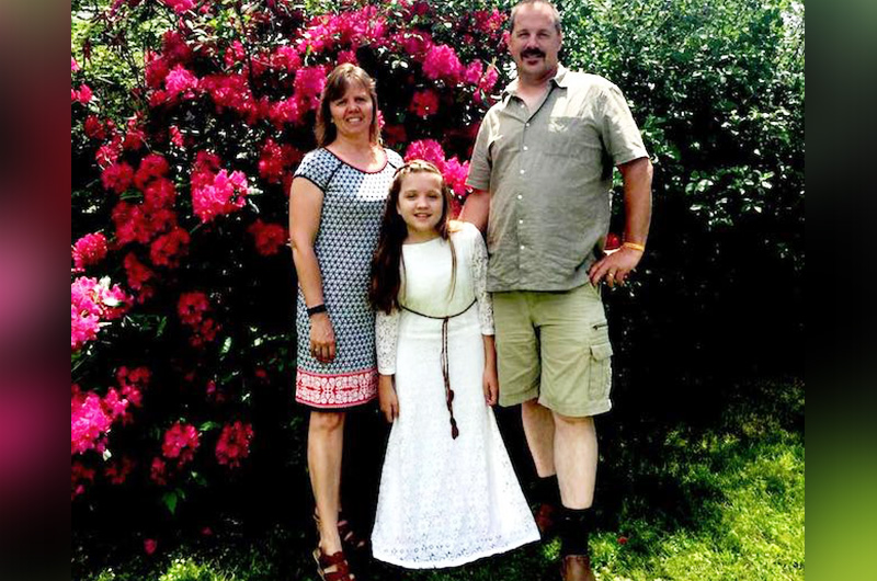 Maria poses with her parents in front of a bright flowering bush.
