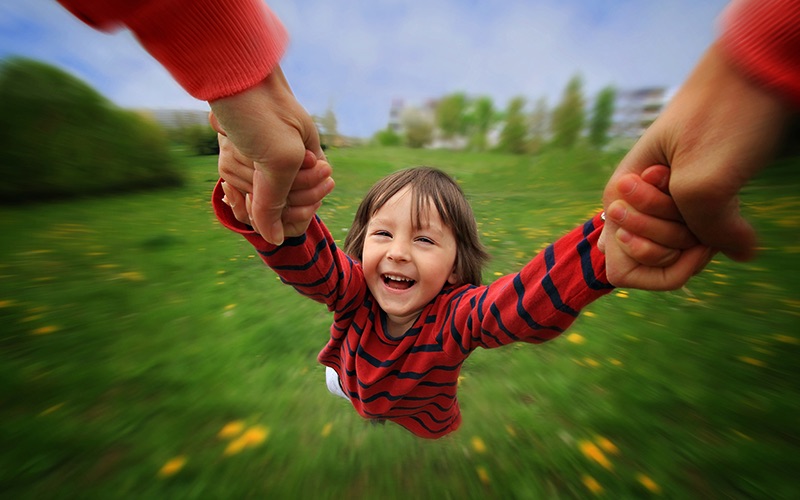 A child being swung in a field by a parent, as the ground spins