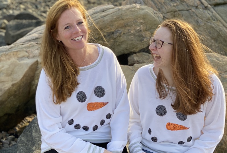 Ava, who has ACM, sits with her mom on a rock jetty at the beach