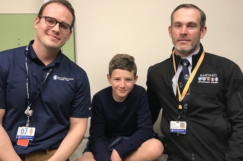 Caden, who had a limb difference caused by a lawnmower accident, sits smiling with his two doctors.