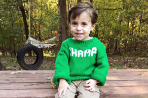 William, who has Pearson syndrome, wears a green sweater that says "Champ"
