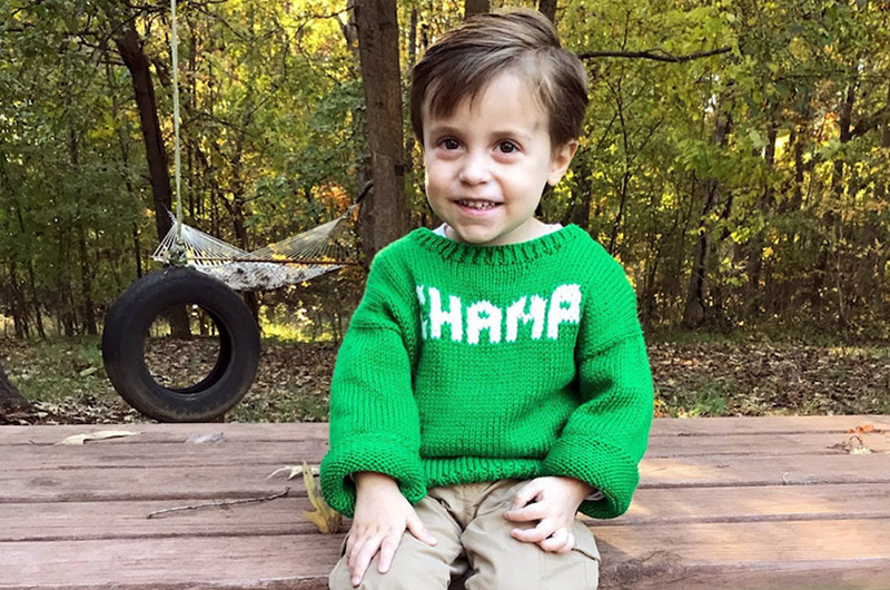 William, who has Pearson syndrome, wears a green sweater that says "Champ"