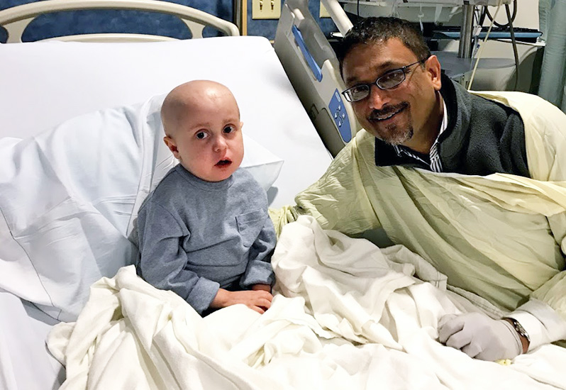 Boy who has Pearson syndrome in his hospital bed following a stem cell transplant, posing with his doctor