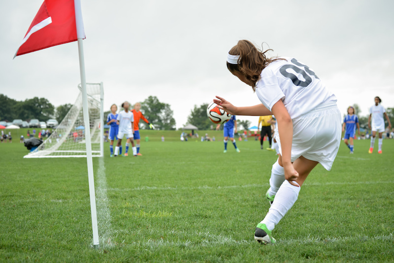Female soccer player kicks the ball back into play from the corner of the field.