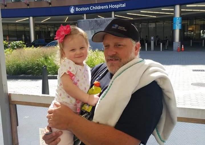 Finley's father, Gary, holds her outside of Boston Children's, where she had surgery for a cavernous malformation.