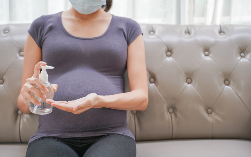 pregnant woman wearing face mask and applying hand sanitizer