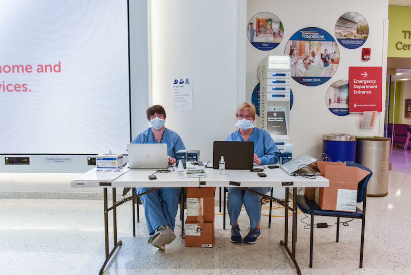 Two women in blue scrubs and face masks at a table in the lobby of Boston Children's during the COVID-19 outbreak