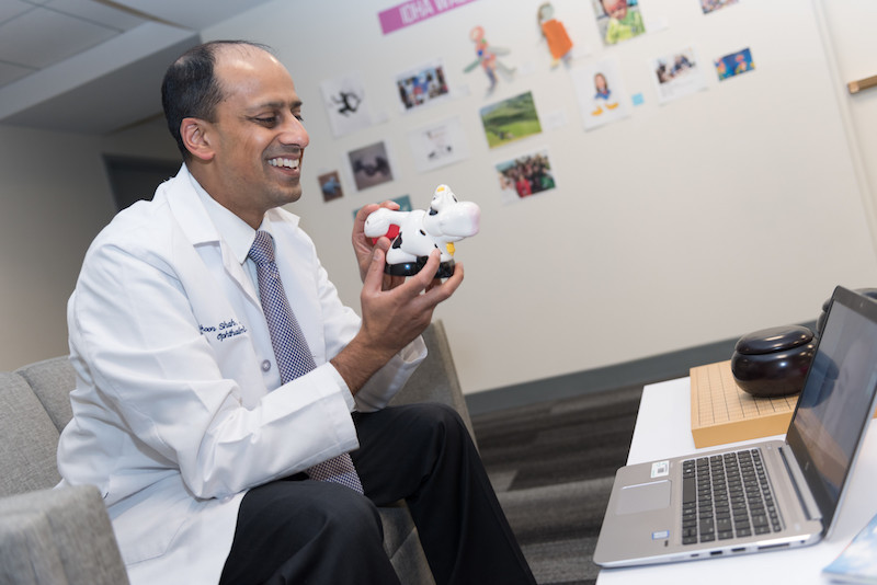 Doctor holds up toy cow as he has a telemedicine visit on his computer