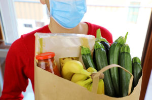Person with mask holds grocery bag of fresh fruit and produce during COVID-19.
