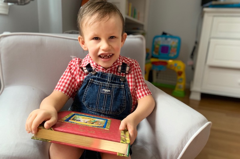 Ian wearing a red shirt and overalls with a book on his lap.