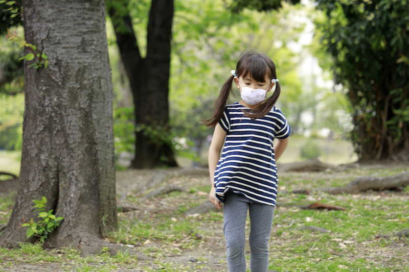 Little girl walking through the woods, wearing a mask
