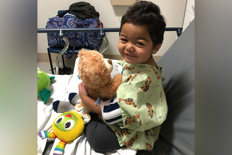 Keith, who has nephrotic syndrome, in a hospital bed, smiling and holding a teddy bear