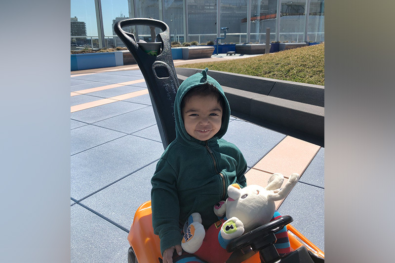 Keith, who has nephrotic syndrome, on a toy car and holding a stuffed animal