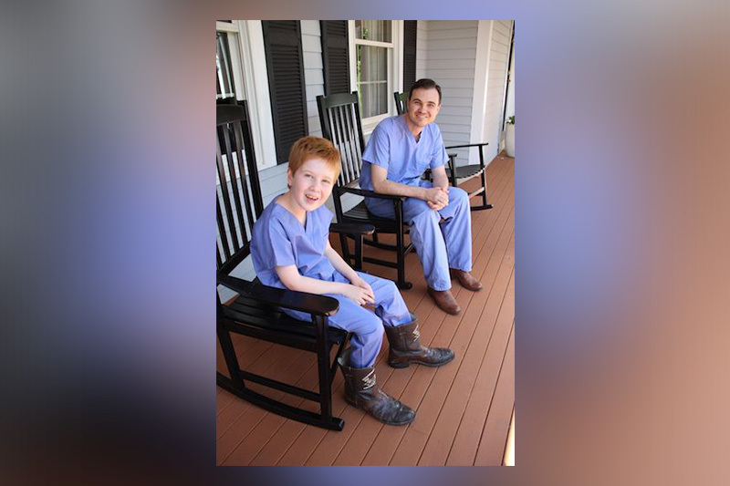 Spine surgeon Grant Hogue and Henry sitting in rocking chairs in scrubs and cowboy boots. 