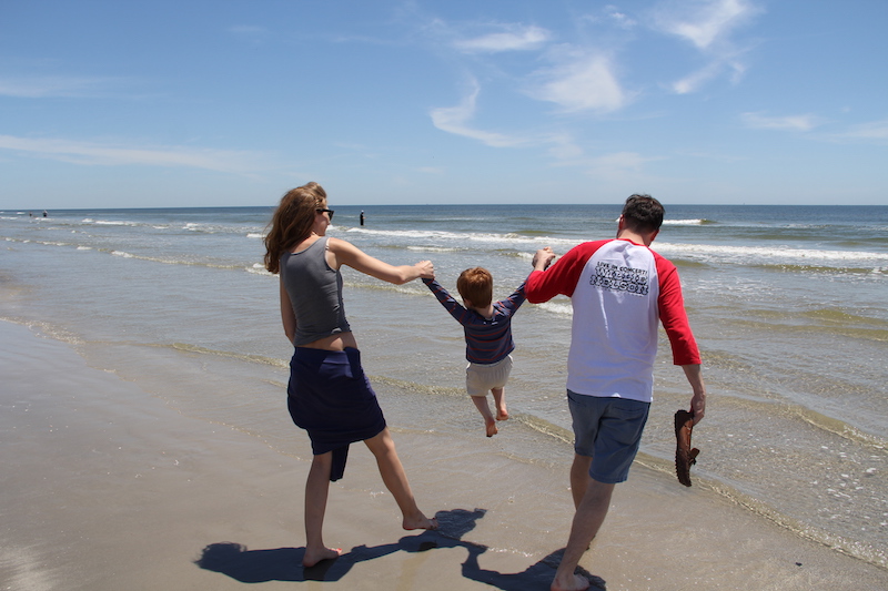 Megan and spine surgeon, Grant Hogue, swing young Henry by the arms over the surf. 