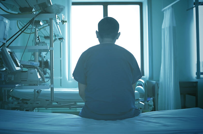 Nurse with PTSD sits in an empty patient room and looks out the window.