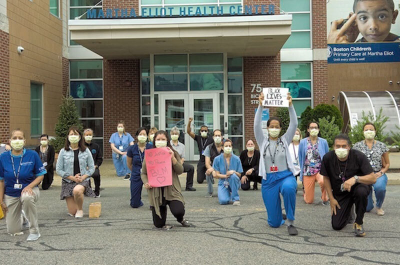 Clinicians wearing masks hold Black Lives Matter signs outside of Martha Eliot Health Center