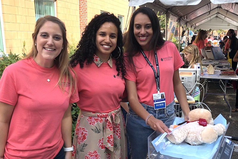 Carla Coutinho and two other nurses, all wearing pink shirts at an outdoor health fair. 