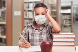 Boy sitting at desk in school wearing mask during COVID-19 outbreak