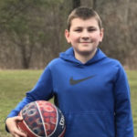 After IBD surgery, a young teen boy holds a basketball outside.
