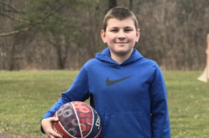 After IBD surgery, a young teen boy holds a basketball outside.