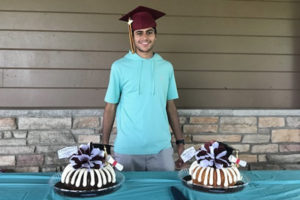 maythum, who had midaortic syndrome, at his college graduation. he has two cakes and is wearing a blue shirt
