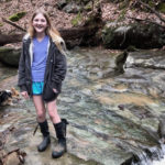 adella stands near a waterfall after recovering from thyroid cancer