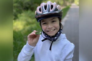 ava, who received car t-cell therapy, waves at the camera. she is wearing a bicycle helmet.