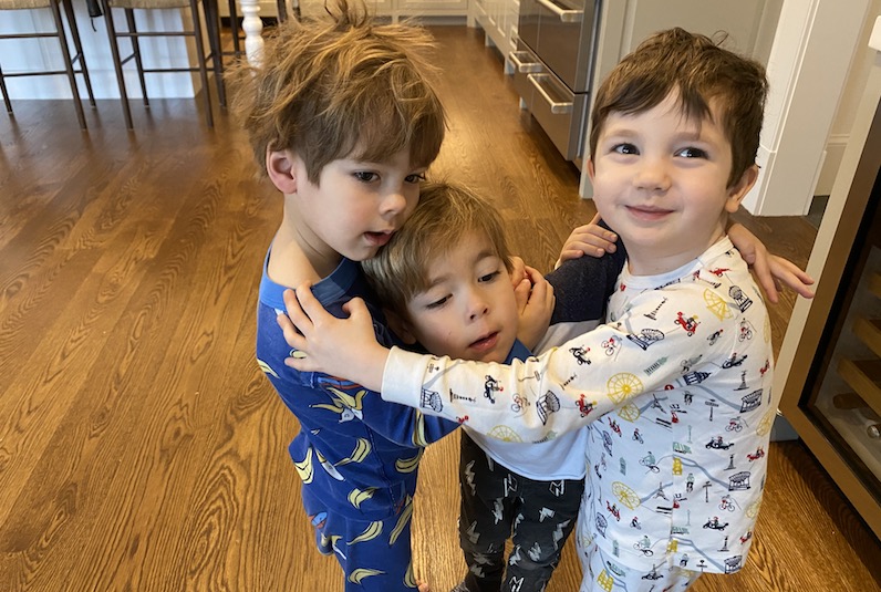 Three boys hug in their pajamas in a kitchen. Two had open heart surgery. 
