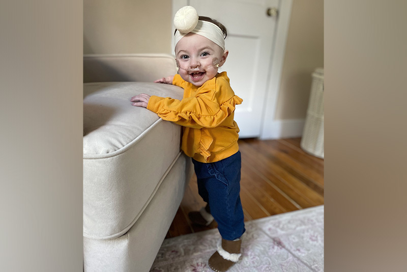 Scarlett, who has CDH, smiles. She is wearing a yellow shirt and a bow in her hair.
