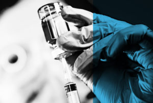 gloved hand holding vaccine bottle and syringe