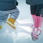 closeup of two pairs of boots walking through snow