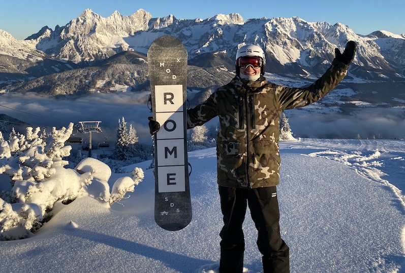 Mikey, who recovered from COVID-19, at the top of ski slope with his snowboard in Austria