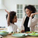 A mother and her child give each other a high five as they prepare food in the kitchen