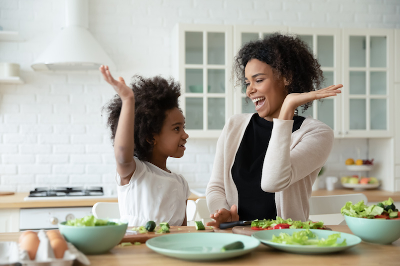 A mother and her child give each other a high five as they prepare food in the kitchen